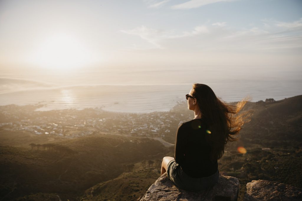 Holiday travellers, South Africa, Cape Town, Kloof Nek, woman sitting on rock at sunset